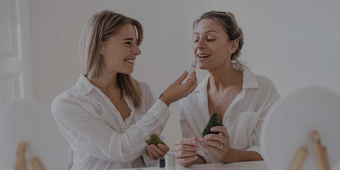 Two women in white shirts applying makeup in a mirror.

