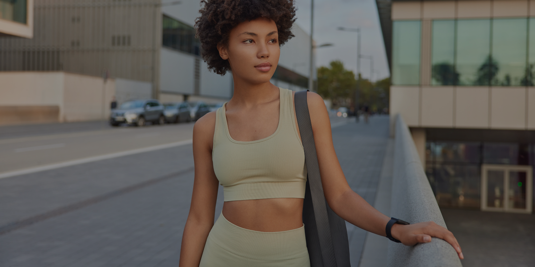 Woman in athletic wear standing on a street with modern buildings in the background

