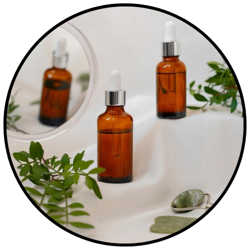 Amber glass bottles with dropper caps on a white surface with greenery

