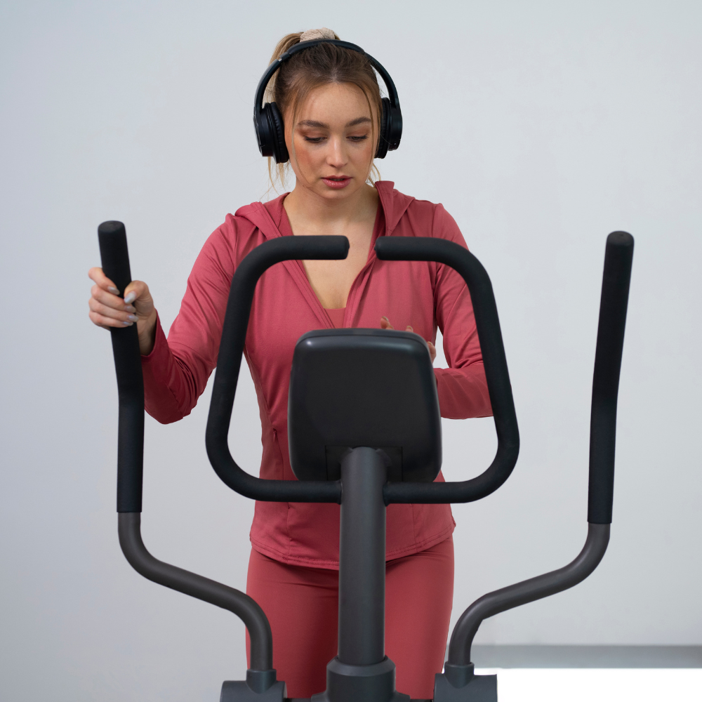 Woman exercising on a cross trainer with headphones on a light gray background

